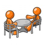 Two orange men at a table consulting over matters.